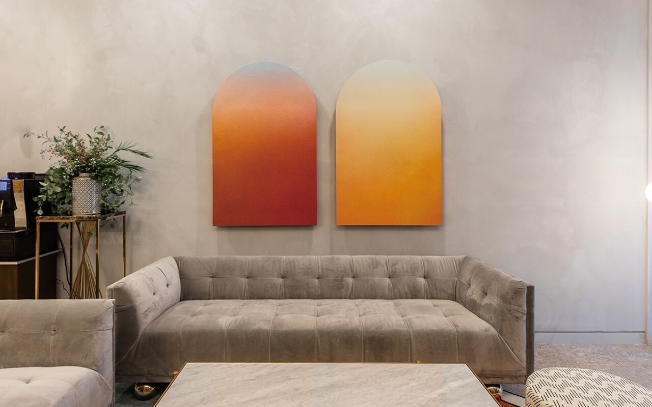 Uma sala de estar moderna com um sofá cinzento, uma mesa de centro e duas obras de arte abstratas nas paredes.