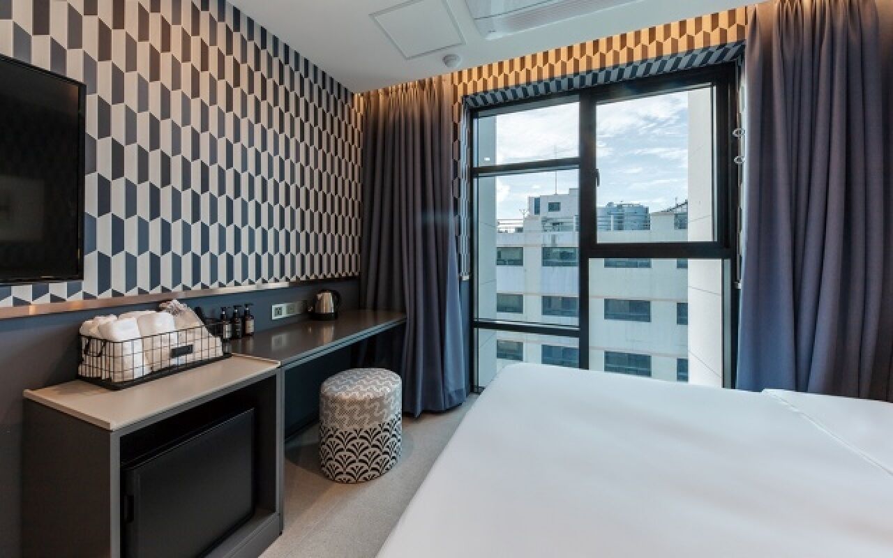 A hotel room with a bed, a desk, a television, and a window with curtains.