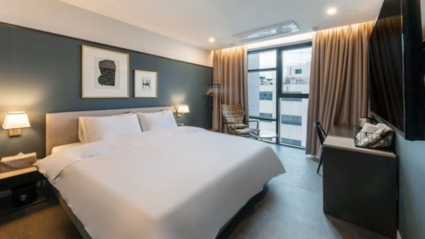 A hotel room with a large bed, a desk with a chair, a window with curtains, and artwork on the wall. - Brown Dot Hotel Deokcheon (Busan)