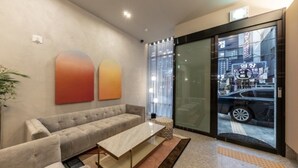 A modern hotel lobby with a sofa, a coffee table, and a large glass door leading to the street. - Brown Dot Hotel Deokcheon (Busan)