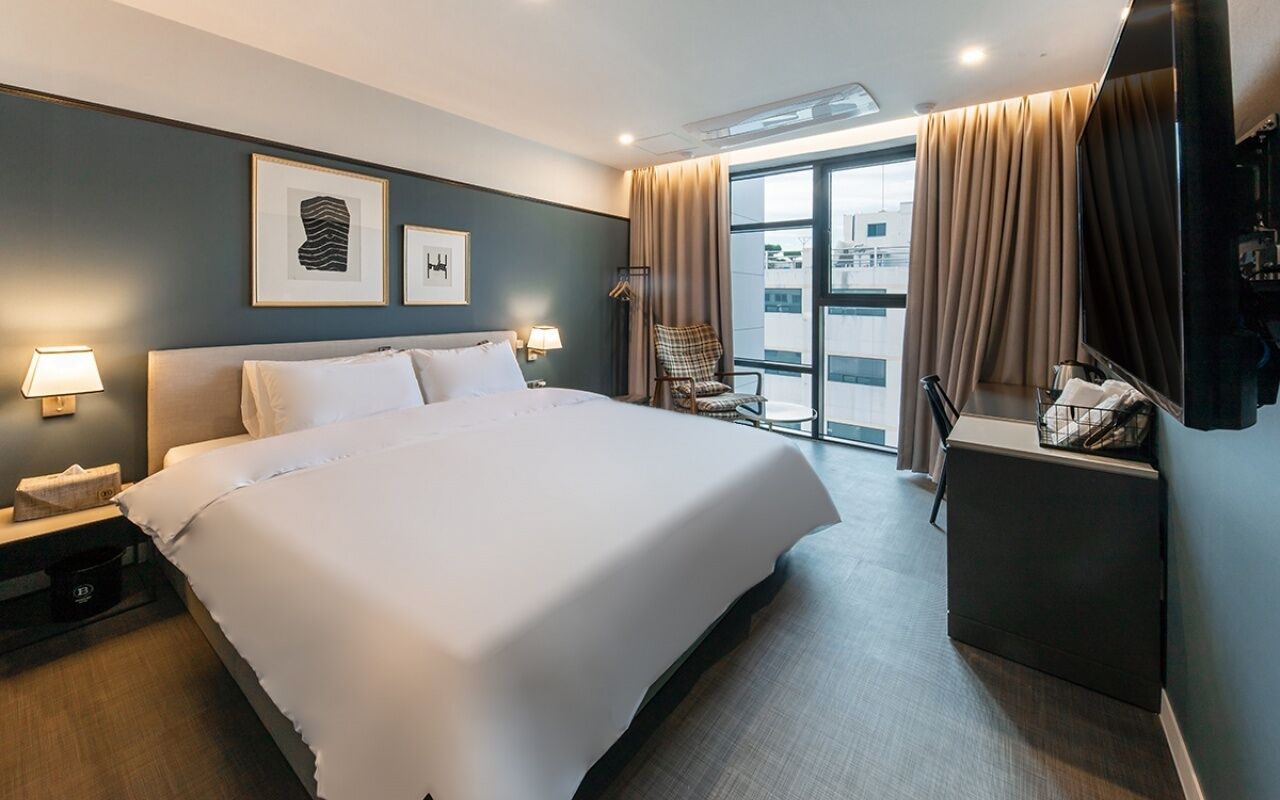 Habitación de hotel con una cama grande, un escritorio, una silla y vistas al exterior.