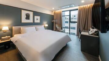 Habitación de hotel con una cama grande, un escritorio, una silla y vistas al exterior.