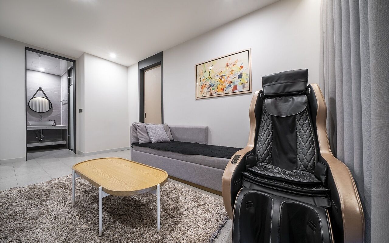 A modern living room with a sofa, a massage chair, a small wooden table, and a painting on the wall.