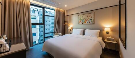 Una habitación de hotel con una cama grande, lámparas de noche, un escritorio con lámpara, una ventana con cortinas y un cuadro en la pared.