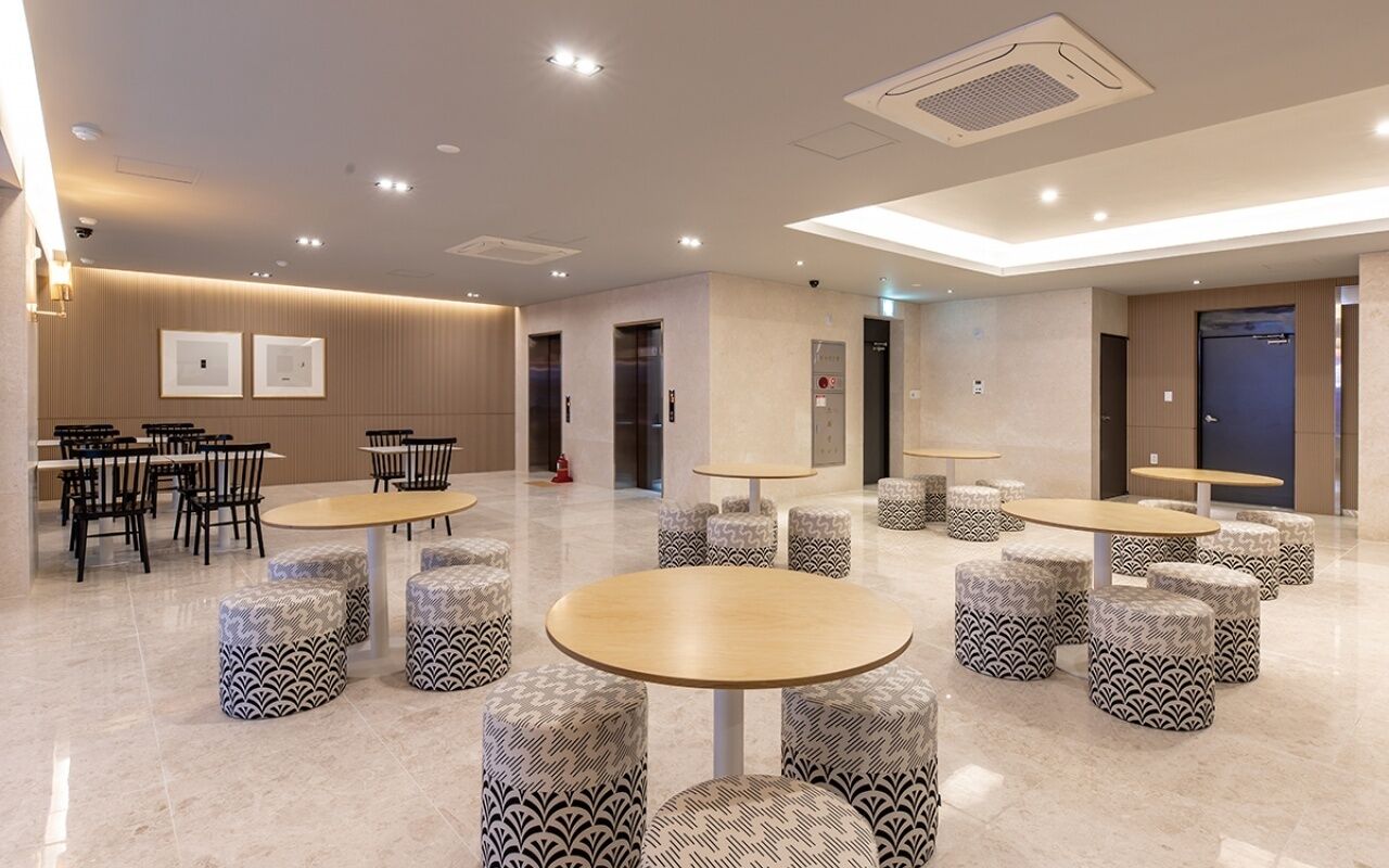 Een moderne hotellobby met ronde tafels, gestreepten poufs en een strak, minimalistisch ontwerp.