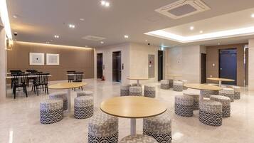 Een moderne hotellobby met ronde tafels, gestreepten poufs en een strak, minimalistisch ontwerp.
