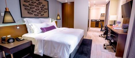 A modern hotel room with a large bed, bedside tables, a desk, and a TV.