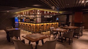Zona de bar con mostrador, taburetes y una nevera pequeña. Mesas y sillas distribuidas alrededor del bar.