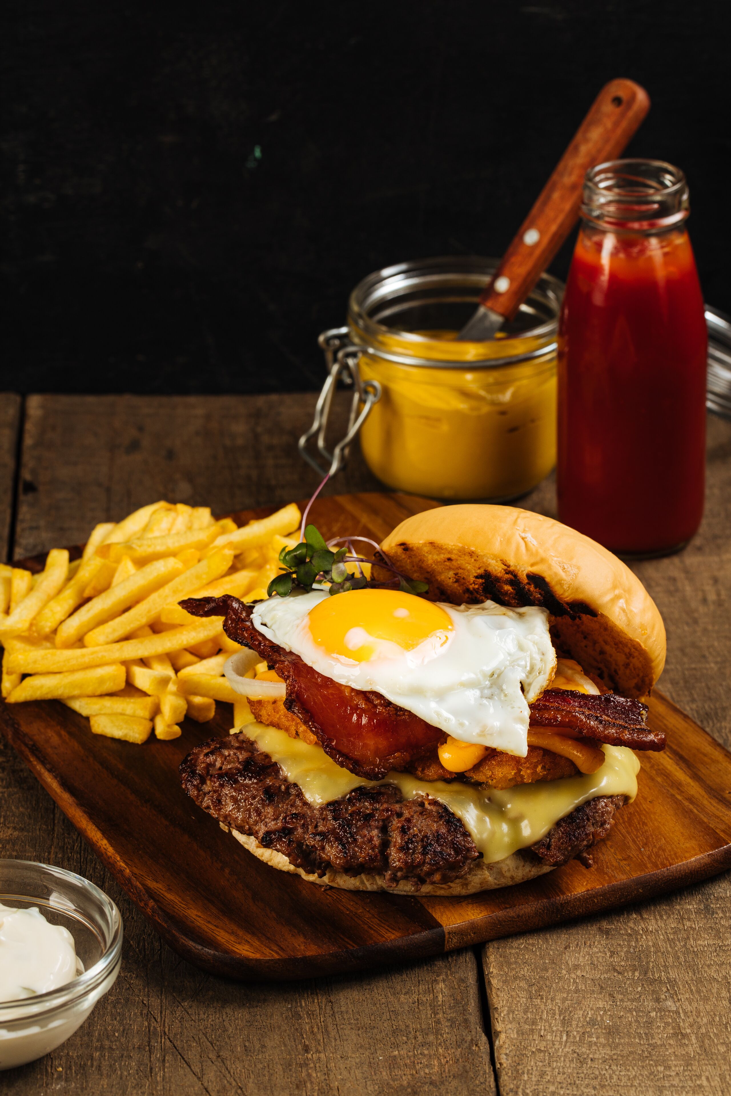 A breakfast plate with a burger, egg, bacon, cheese, and fries.