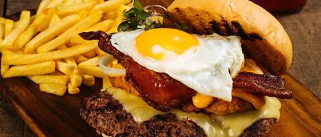 Un plato de desayuno con hamburguesa, huevo, tocino, queso y papas fritas.