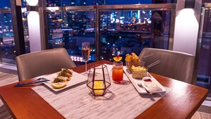Una mesa de comedor con vista a la ciudad, platos de comida, una bebida y una vela.