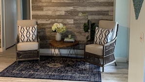 A room with two armchairs, a small round table with a vase of flowers, and a wooden accent wall.