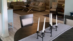 A modern living room with a large window, a sofa, a dining table with candles, and a chandelier.