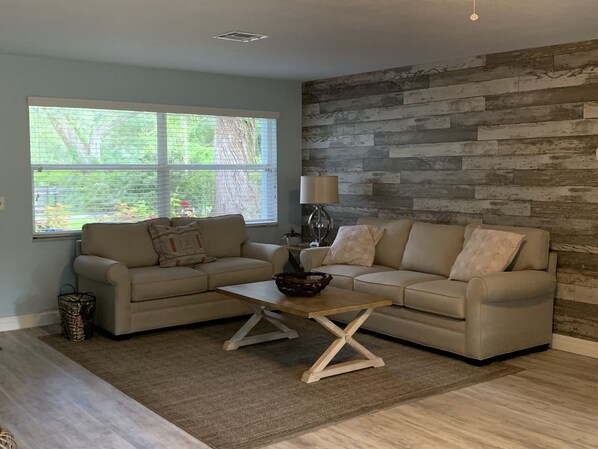 A living room with two sofas facing each other, a coffee table, a lamp, and a window with blinds. - 3/3 ON WEEKI WACHEE RIVER (Weeki Wachee)