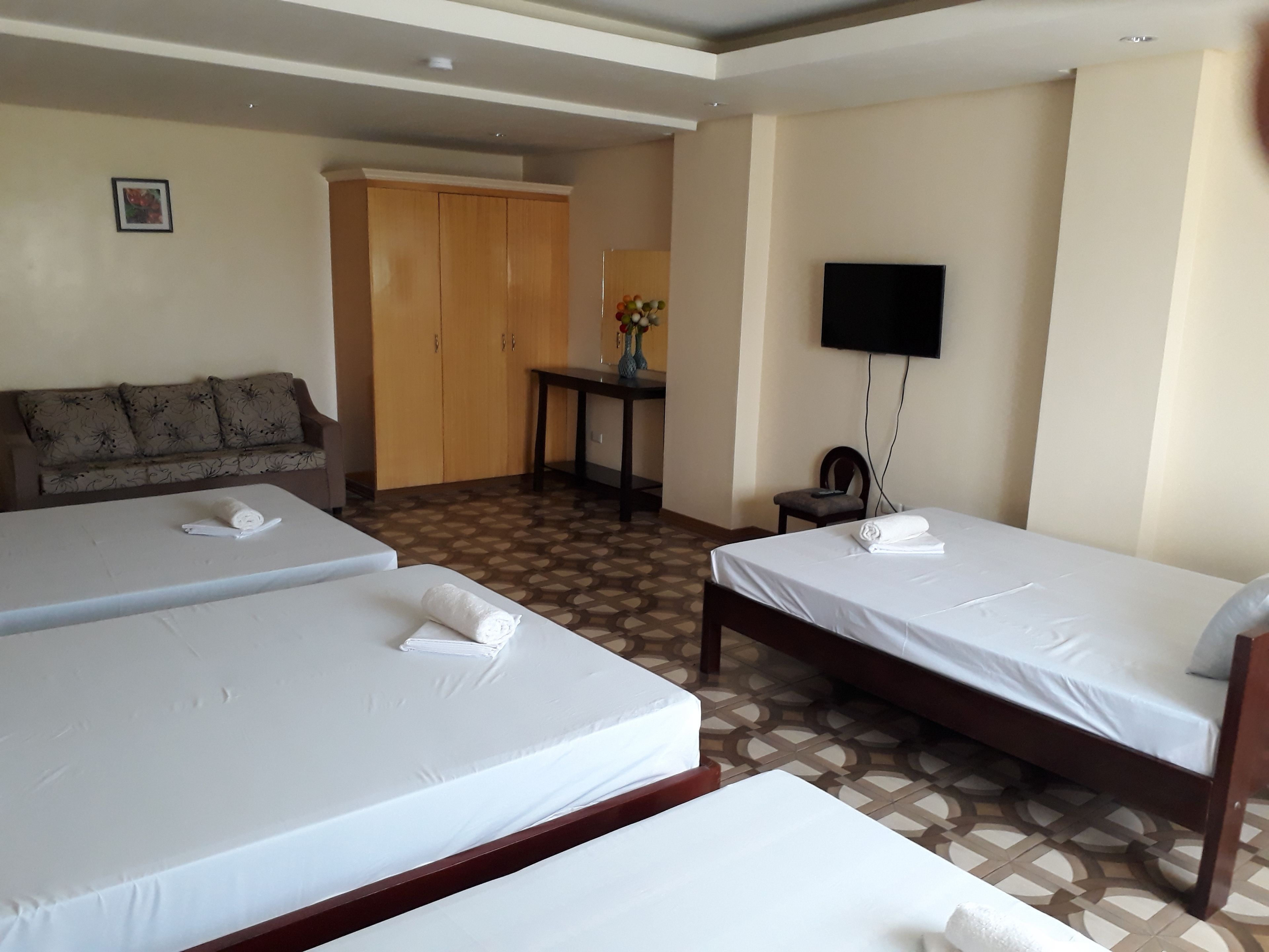 Habitación de hotel con dos camas, un sofá, un televisor y un escritorio con un florero.