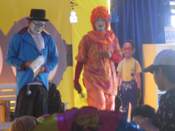 Un escenario con dos artistas disfrazados, un niño al fondo y un público en primera fila.