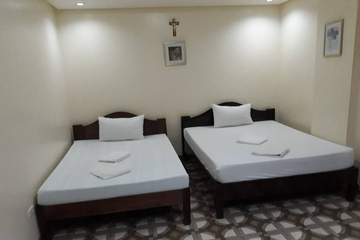 A hotel room with two beds, each with a white mattress and pillow, a wooden headboard, and a patterned floor.