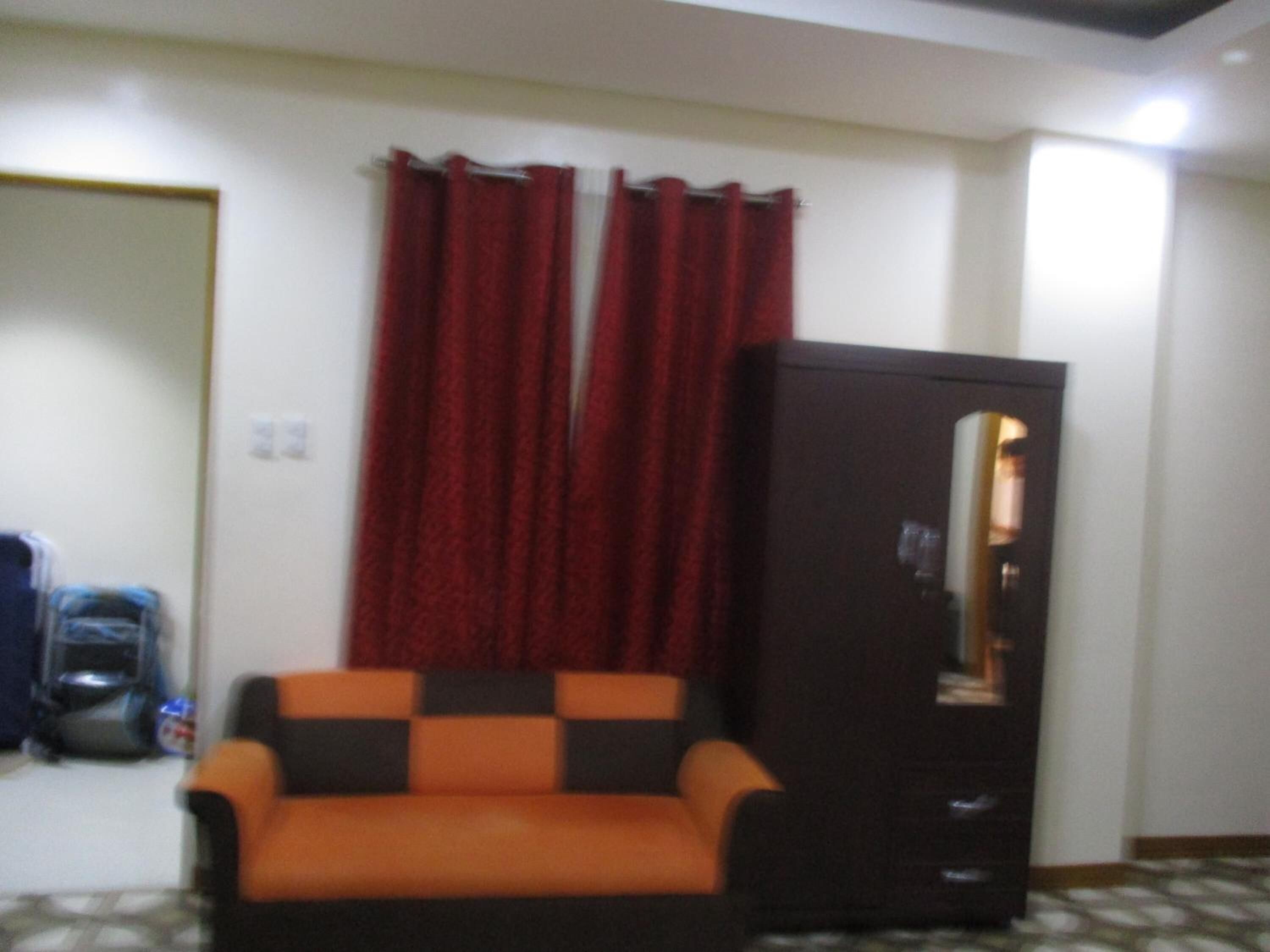 Una habitación con sofá, armario y ventana con cortinas rojas.