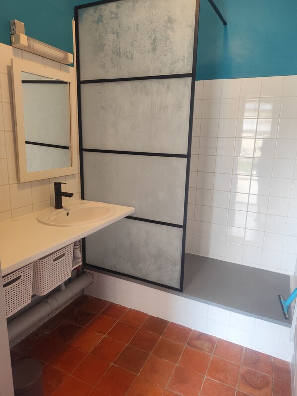 A bathroom with a white sink, a mirror, a shower enclosure, and a tiled floor. - Welcome to casa T3. Apartment in the heart of the village of Giffaumont-Champaubert. (Giffaumont-Champaubert)