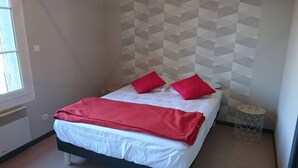 Ein Einzelbett mit weißer Bettwäsche und roten Akzenten, ein kleiner runder Nachttisch und eine Wand mit geometrischem Muster.