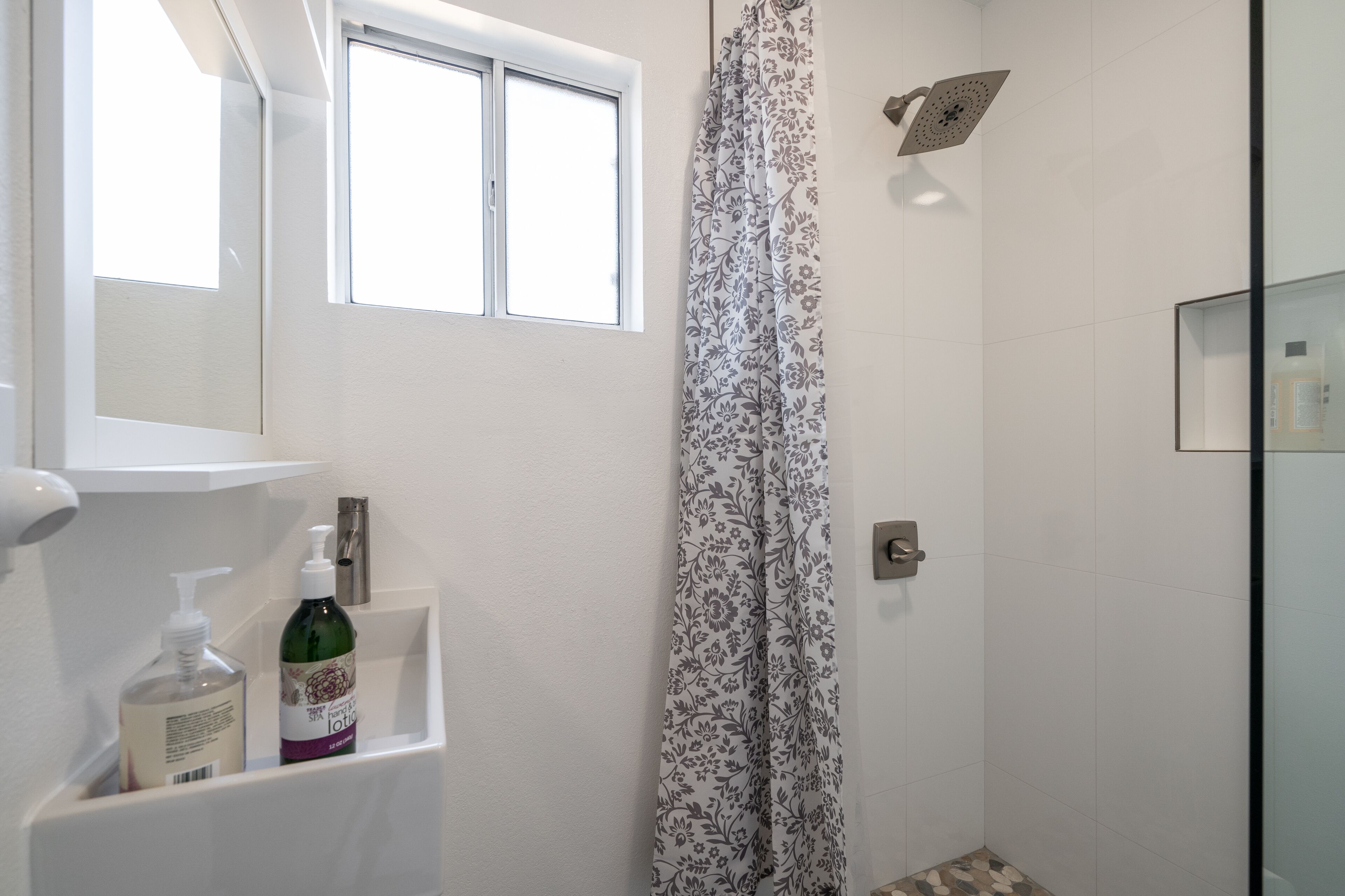 Un baño con ducha, una ventana y un estante con artículos de aseo.