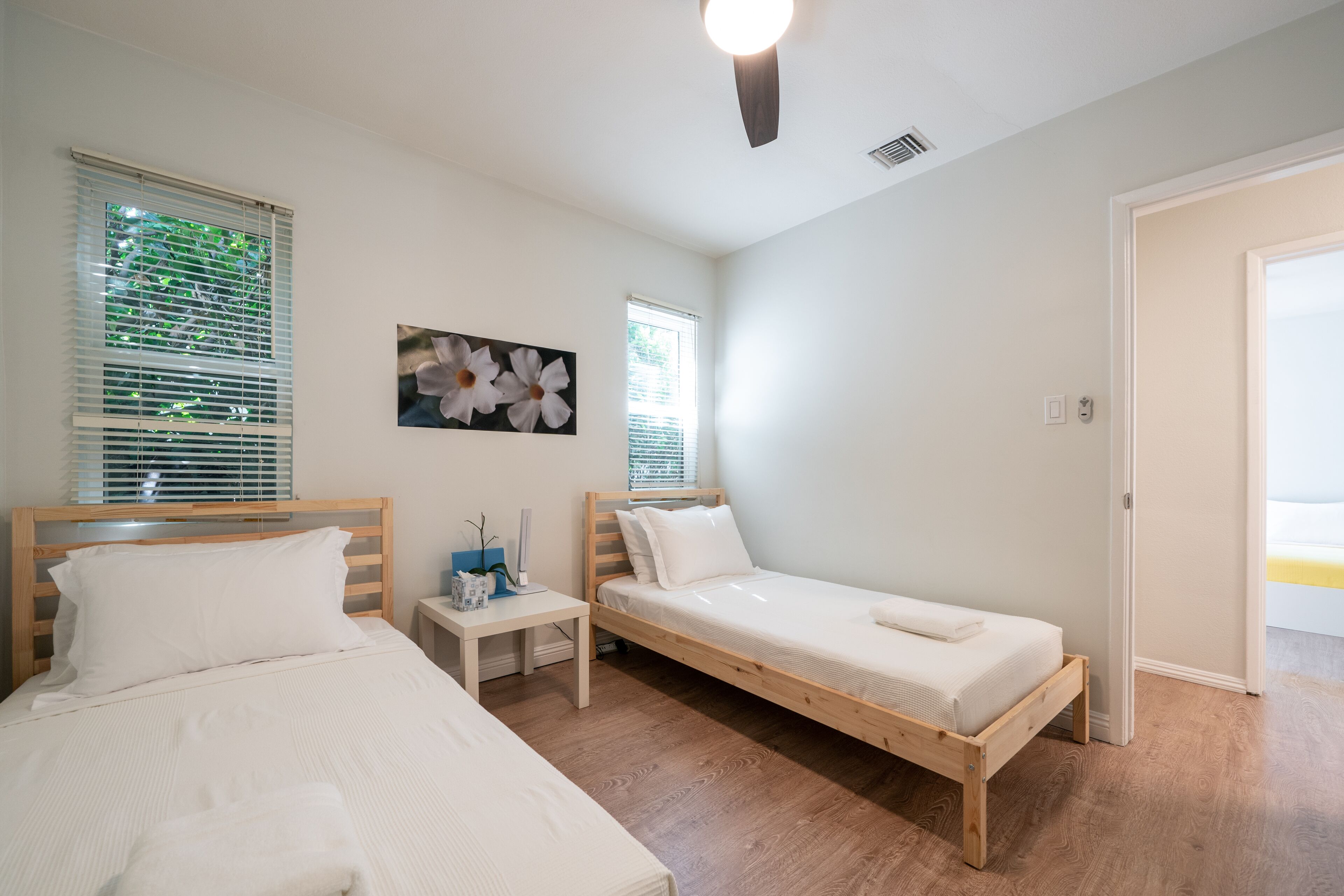 Un dormitorio con dos camas individuales, una mesita de noche con lámpara y una ventana con persianas.