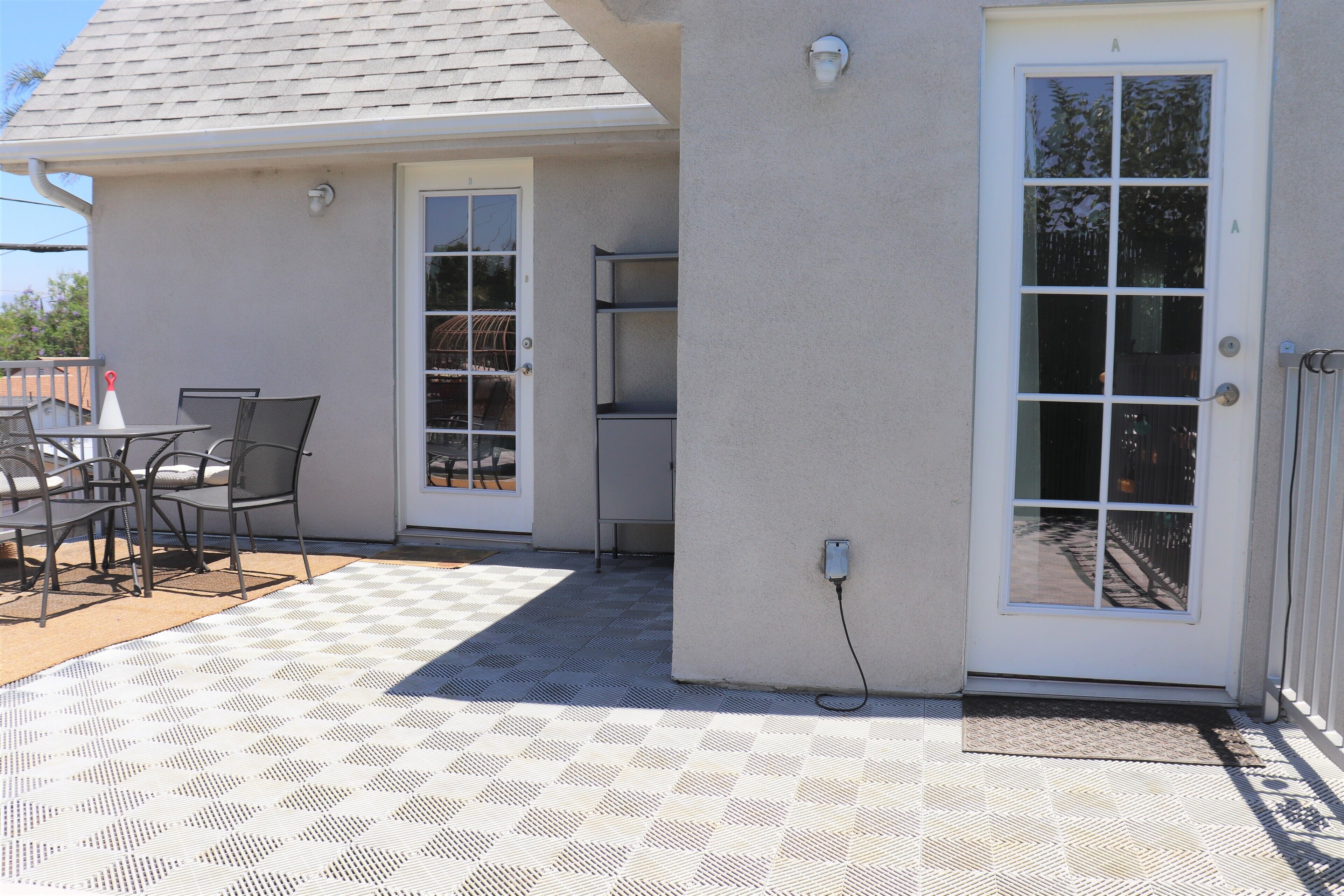 Une terrasse avec un sol à carreaux, une table entourée de chaises et une porte dotée d’une fenêtre.