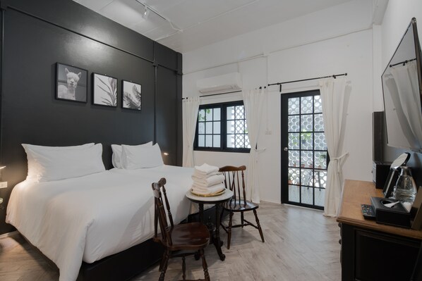 Habitación de hotel con una cama grande, dos sillas, una mesita con toallas, una cafetera y vistas a través de una ventana con cortinas.
