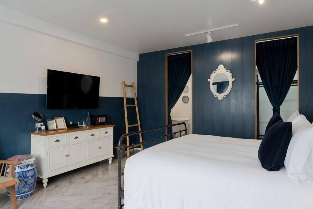 Een slaapkamer met een bed, een kapstok, een televisie, een spiegel en een raam met gordijnen.