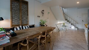 A spacious living area with a wooden dining table, cushioned chairs, a staircase, and a potted plant. - Blu Monkey Boutique Phuket Town (Phuket)