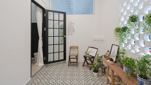 A small room with a tiled floor, a wooden chair, a table with plants, and a wall with a geometric pattern. - Blu Monkey Boutique Phuket Town (Phuket)