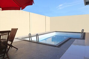 Relax by the pool surrounded by a low wall and a comfortable lounge chair.