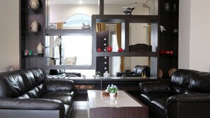 A modern living room with two black leather sofas, a wooden coffee table, and a decorative mirror above a shelving unit. - OYO 1326 Mahakam Guest House (Padang)