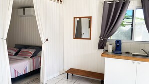 Une chambre à coucher avec un lit, une table de chevet avec une bouilloire, un miroir et une fenêtre avec des rideaux.