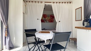 Une pièce compacte comprenant une table et des chaises, un petit coin cuisine et un lit doté d’une tête de lit à motifs floraux.