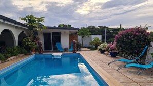 Une piscine rectangulaire avec une terrasse carrelée, entourée de plantes en pot et agrémentée d’une pergola en bois.