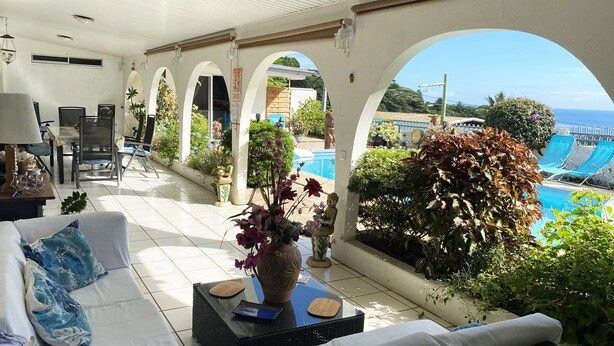 Une terrasse ensoleillée avec une piscine, des arches blanches et un canapé agrémenté de coussins.