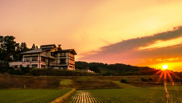 A modern two-story house with a symmetrical design, situated on a hillside overlooking a cultivated field. - Yasuragiso (Joetsu)