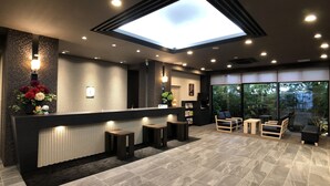 A modern reception area with a skylight, a reception desk, seating, and a view of greenery outside. - Hotel Route-Inn Grand Ota Ekimae (Ota)