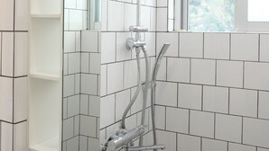 A modern bathroom with white tiles, a shower with a handheld showerhead, a glass-enclosed window, and a mirror. - Casa Botanika (Yomitan)