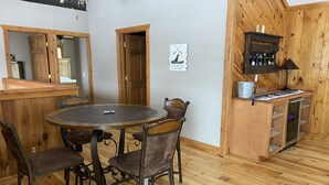 Un interior de madera con una mesa redonda y cuatro sillas, un armario de madera con botellas y un letrero en la pared.