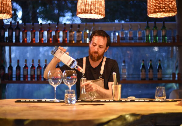 Un cantinero sirviendo una bebida en un vaso, en un bar con una variedad de botellas al fondo.