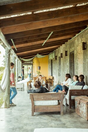 A covered outdoor seating area with wooden benches and tables, a concrete floor, and a rustic wall. - Estancia Anastasio by Folk (Maldonado)