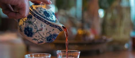 A hand pouring tea from a blue and white patterned teapot into a glass on a red tray.
