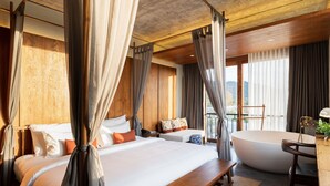 A bedroom with a large bed, a separate sofa, a bathtub, and a balcony with a view.