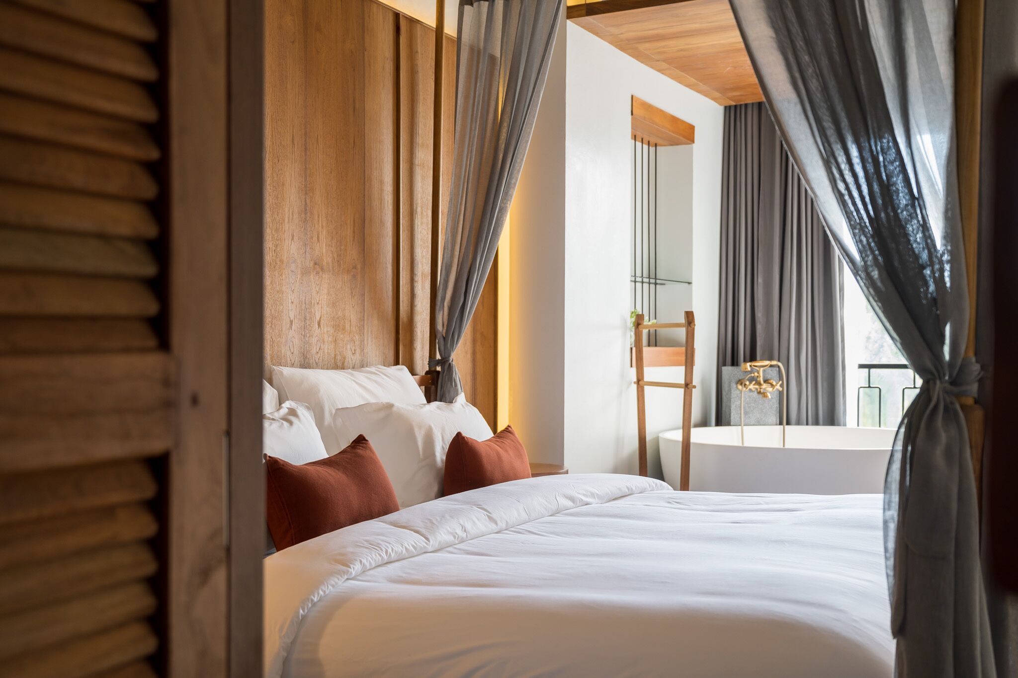 Een hotelkamer met een groot bed, houten lambrisering, een badkamer met bad en grijze gordijnen.