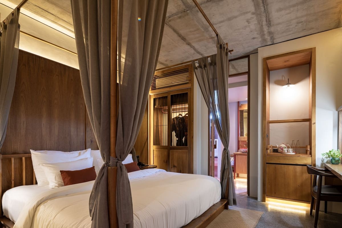 A bedroom with a canopy bed, wooden walls, a small desk, and a view into another room.