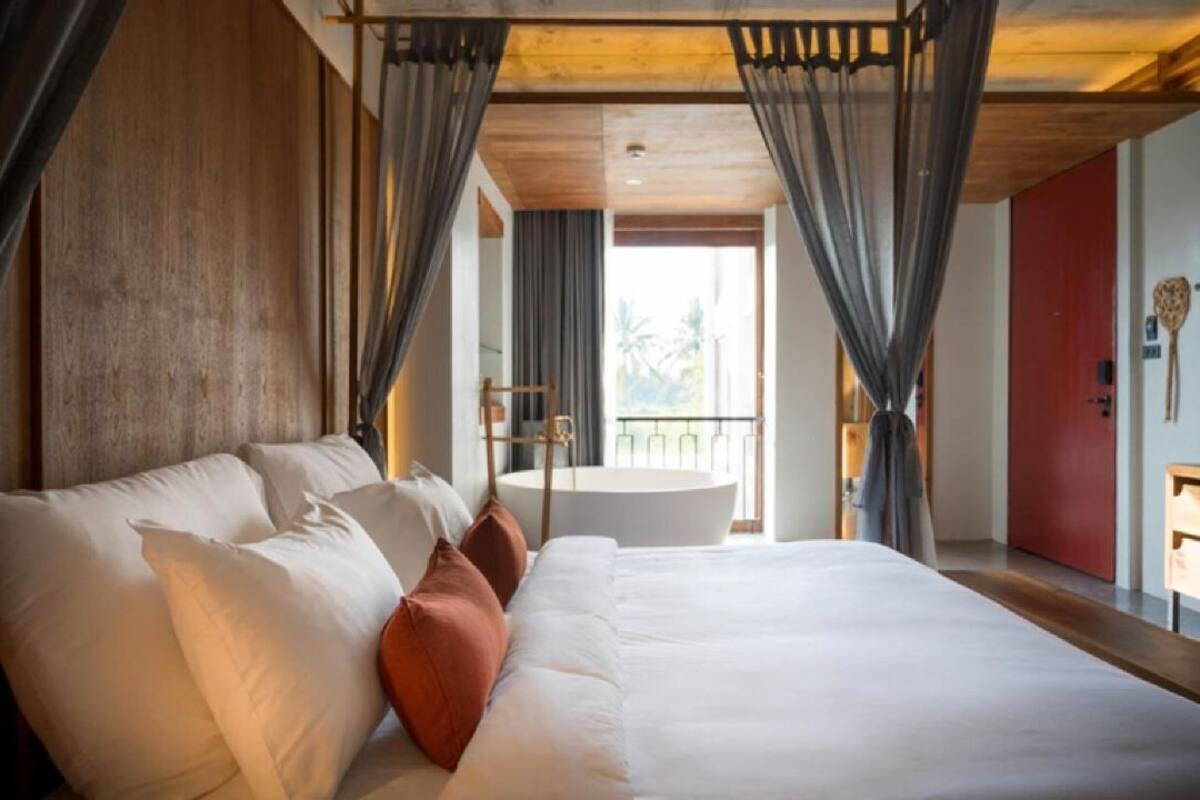 A modern bedroom with a large bed, a round bathtub, and a balcony with a view.