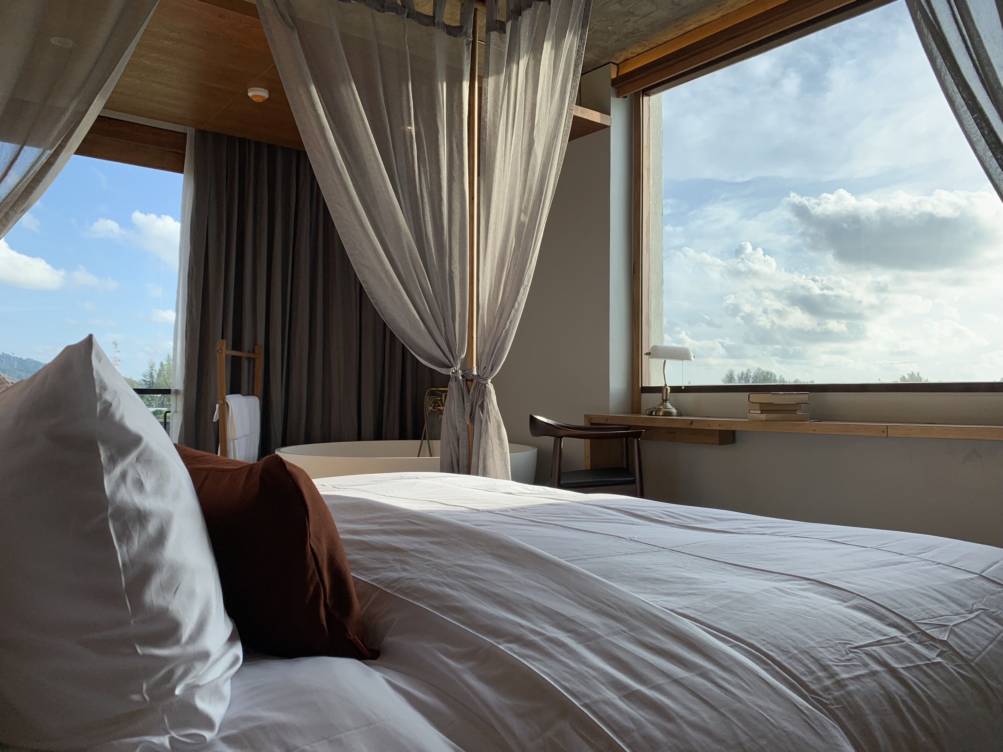 A bedroom with a bed, a desk, and a window with curtains.