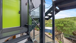 Un edificio moderno con una puerta verde brillante, una escalera con barandillas de vidrio y vistas a un área ajardinada.